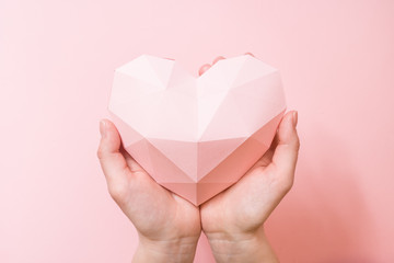 Hands holding a paper polygonal pink heart