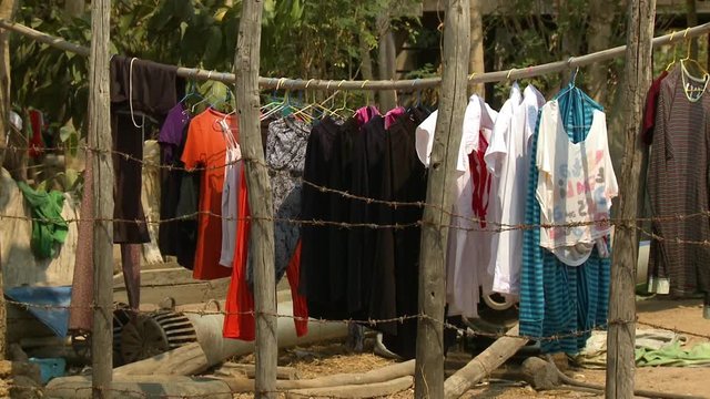 A daylight medium shot of various clothing in a multitude of colours hanging at the clothesline behind a barbwire fence on a sunny day.