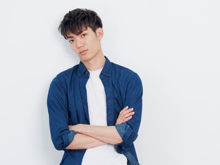 Portrait of a handsome Chinese young man in blue shirt looking at camera with two arms crossed, serious expression, isolated on white background.
