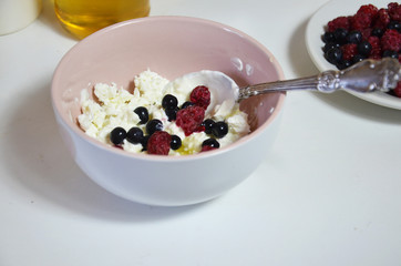 Ricotta with fresh berries and honey on white table. Cottage cheese, curd cheese or tvorog with berries in bowl. Summer dessert, breakfast or healthy snack. jar of honey blueberries and raspberries