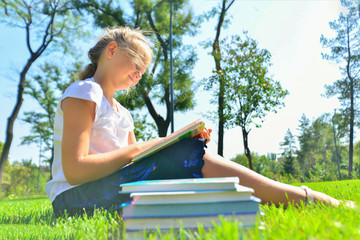 A girl teaches assignments on textbooks and sits on the green grass in the park.