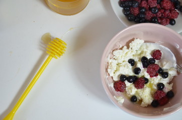 Ricotta with fresh berries and honey on white table. Cottage cheese, curd cheese or tvorog with berries in bowl. Summer dessert, breakfast or healthy snack. jar of honey blueberries and raspberries