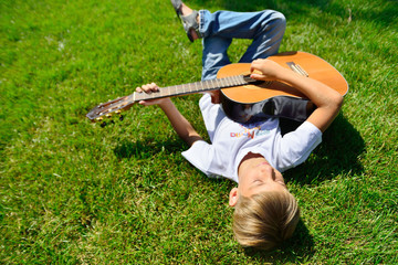 A young musician is lying on the green grass with a guitar in his hands, top view.