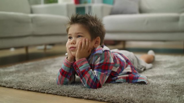 Boy carefully watches cartoons on TV lying on the floor in living room