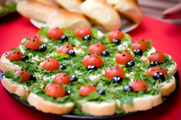 plate with small sandwiches on which there are edible figurines of ladybugs from tomato and olives