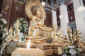 Golden buddha status is in buddhist hall and candle flame in foreground at Wat Chana Songkram, Thai temple in Bangkok Thailand.