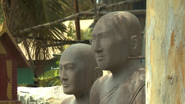 A daylight closeup shot of several large human statues with no hair carved from stones on display in an outdoor setting in the village of San Tok, Cambodia.