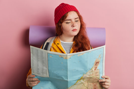 beautiful stylish female hiker looking at map isolated on pink background. close up photo. travel, lifestyle, free time, spare time, leisure