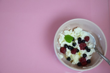 Ricotta with fresh berries and honey on pink table. Cottage cheese, curd cheese or tvorog with berries in bowl. Summer dessert, breakfast or healthy snack. jar of honey blueberries and raspberries