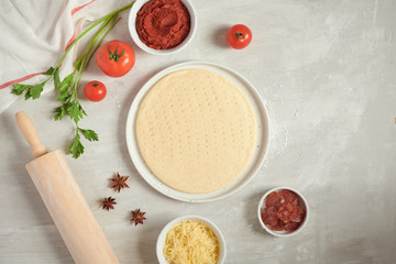 Fresh dough pizza base and ingredients on a white table. Top view.