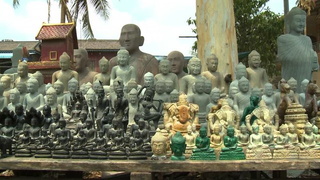A daylight closeup shot of a wide range and styles of Buddha and other Buddhist ornamentations carved from various types of stones, taken in an outdoor setting in the village of San Tok, Cambodia.