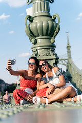 Cheerful women sitting on bridge and using cellphone