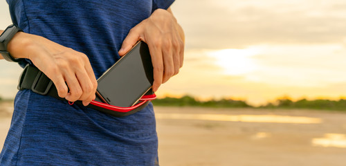 Young Asian woman keep smartphone in waist bag before running cardio exercise in the morning....