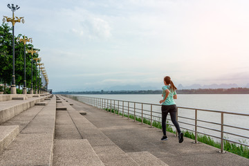 Young woman running on the street with a view of the river in the morning.