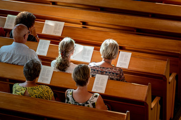 Poeple singing worship songs at wooden bench in church with soft sun light.