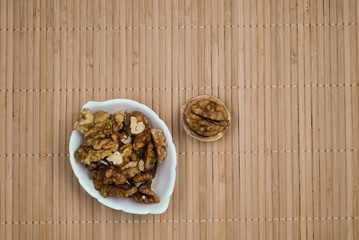 Close-up of half a walnut and a white plate with walnut kernels on a warm wooden background