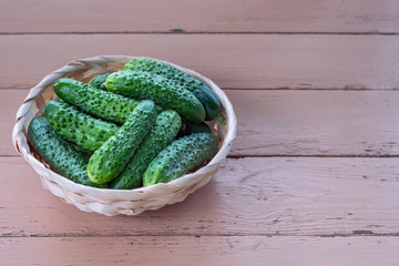 Top view of fresh cucumbers in a wicker bowl on a wooden table. Healthy food concept
