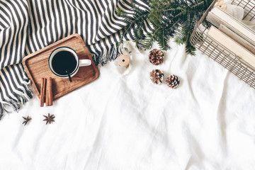 Christmas styled composition. Cup of coffee, plaid, old books in golden basket, pine cones, fir branches on white table, linen background. Flat lay, top view. Winter holiday lifestyle concept, web