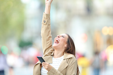 Excited woman holding phone celebrating good news outdoors