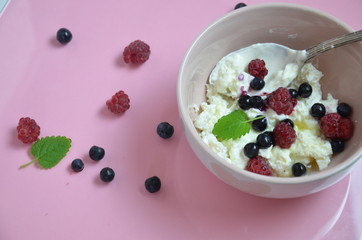 Ricotta with fresh berries and honey on pink table. Cottage cheese, curd cheese or tvorog with berries in bowl. Summer dessert, breakfast or healthy snack. jar of honey blueberries and raspberries