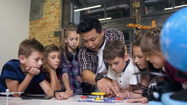 Creative children with teacher launching electronic constructor with fan and turning flashlight . Creative pupils with teacher working on t he tech project at school