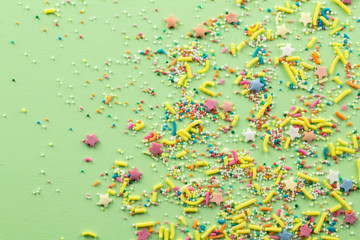 Sprinkles on pale green background - Assorted colourful cake topping sprinkles sprayed on green on bottom corner with space for text - top view of star shapes, dots and oblong sprinkles