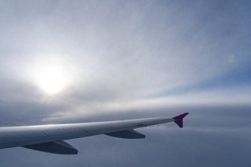 Up in the air, view of aircraft wing silhouette with dark blue sky horizon and cloud background in sun rise time, viewed from airplane window