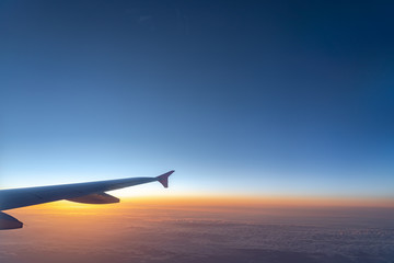 Up in the air, view of aircraft wing silhouette with dark blue sky horizon and cloud background in sun rise time, viewed from airplane window