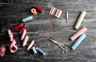 Spools of thread , needles and pins , sewing tools lie on black wooden board