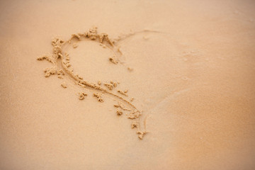 Heart on the beach. Heart in the sand. Draw on the yellow sand with  finger.  Symbol of love. Half heart with blur