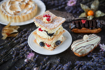 Tea and sweets on a dark background, Mille-feuille, Eclairs, Tart, Decorative with flowers, Selective focus, Closeup