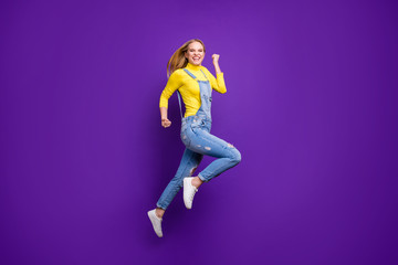 Fototapeta na wymiar Full size photo of cheerful girl raising her fists screaming yeah wearing yellow turtleneck denim jeans isolated over purple violet background