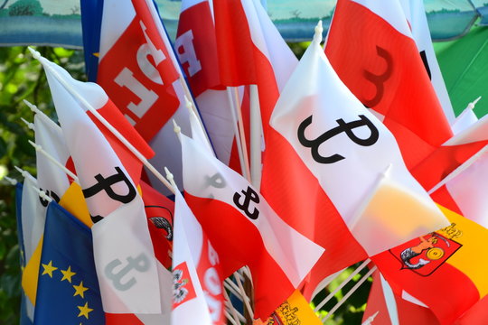 Flags of Warsaw with mermaid, Flags of Poland with Anchor (polish: Kotwica) - symbol of Fighting Poland from Warsaw Uprising and European Union Flag. Flags for sale on souvenir stand. Closeup.