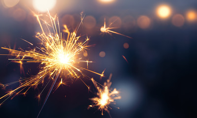 Glittering burning sparkler against blurred bokeh light background - Powered by Adobe