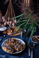 Sweet pasta dessert, noodles with poppy seeds, plum compote from fresh plums, dark background, blue table decorated with fresh flowers. Dry whole poppy plant in background.