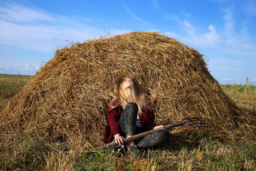 Naklejka na ściany i meble Very tired cute girl, resting sitting on the hay with a pitchfork in her hands, after hard work in the field.