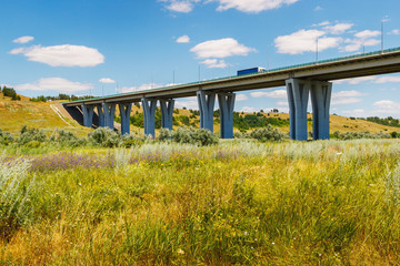 The big modern bridge with a semi truck on it and green field under it. Highway M4 