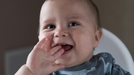 Adorable happy baby boy is looking into the camera. The baby looks around and then smiles and laughs. 1 year old child with brown eyes smiles at home