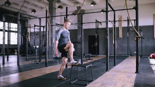Athletic man does box jumps in deserted factory gym. Making endurance and stragth better. Intense exercise is part of daily cross fitness training program. Jymping exersice on metal box.