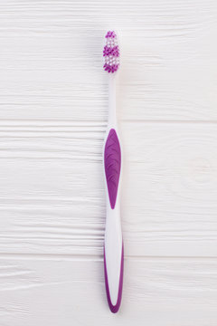 Purple tooth brush on white wooden background. New plastic tooth brush, top view.