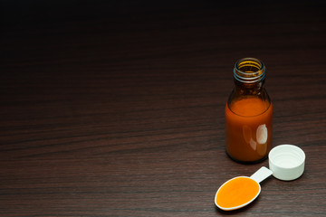 Syrup medicine in a medication bottle and medication spoon on a dark brown wooden desk. Cough and...