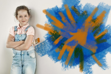 Little girl makes repairs in blue overalls. The child paints the walls with blue and orange paint....