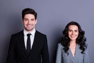 Portrait of charming couple of freelancers looking with toothy smile having brunette wavy curly hairstyle wearing black tuxedo blazer jacket isolated over grey background