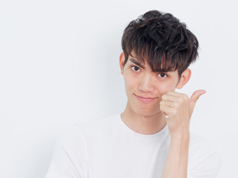 Portrait of a handsome Chinese young man in white t-shirt looking at camera with thumbs up gesture, smiling and happy expression, isolated on white background.