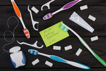 Dentist appointment message and tooth care products. Dentist appointment card, toothbrush, dental floss and chewing gums on black background.