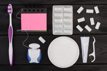 Dental care items on black background. Toothbrush, dental floss, teeth cleaning powder and spiral notepad. Dental health concept.