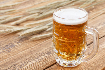Glass of beer with ears of barley on a wooden background.
