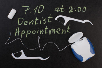 Note dentist appointment and dental floss. Reminder dentist appointment on chalkboard and dental...