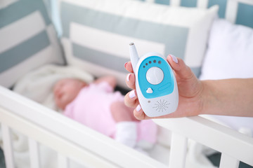 Mother holding radio nanny near bed with sleeping baby