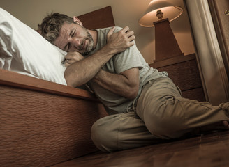 young depressed and desperate man sitting on bedroom floor next to bed suffering depression and...